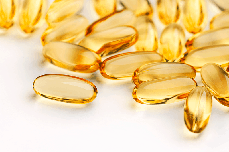 a close-up shot of golden yellow fish oil capsules on a white table top