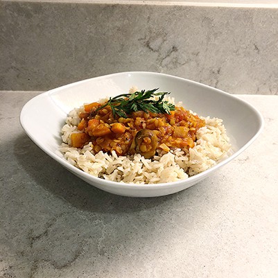 white square bowl filled 1/2 way with brown basmati rice topped with a golden lentil chili and a sprig of mint on top