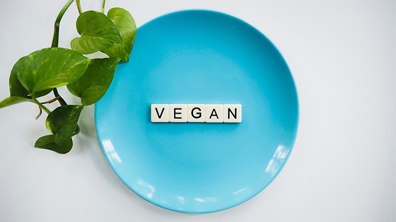looking down on a teal blue plate that has scrabble tiles spelling VEGAN in the center of it